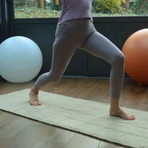 Personne en posture de fente haute sur un tapis de yoga en laine