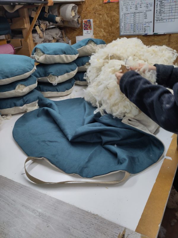 Remplissage de laine locale dans une écocotte en lin lors de la fabrication en atelier